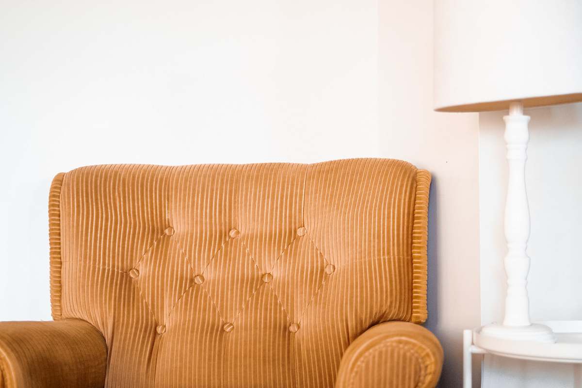 pillow tufted brown fabric sofa chair beside white table lamp on white end table furniture
