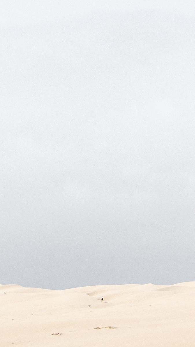 Capture the essence of solitude with this stunning image of a lone man walking across a vast, untouched sand dune. The golden grains of sand stretch endlessly under a clear blue sky, evoking feelings of peace and exploration. This scene is perfect for travel blogs, adventure-themed content, or any project that seeks to convey freedom and the beauty of nature's desolation.