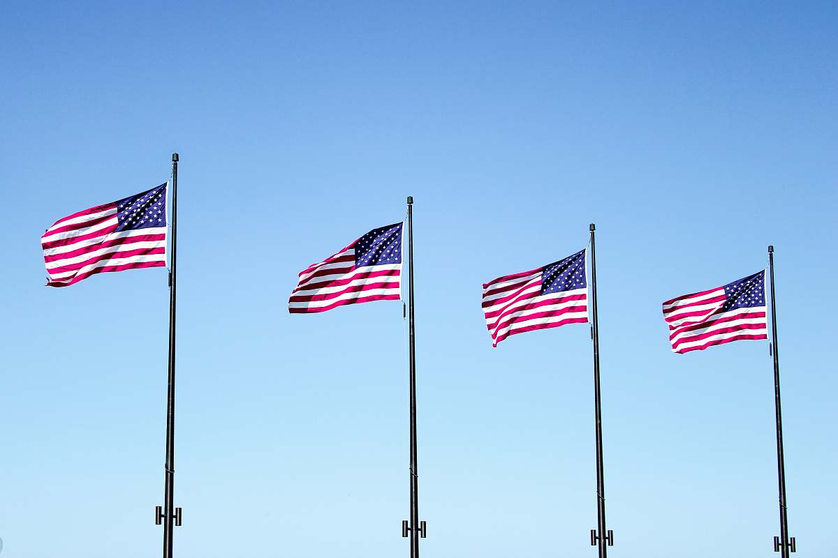 emblem four USA flags under blue sky pole