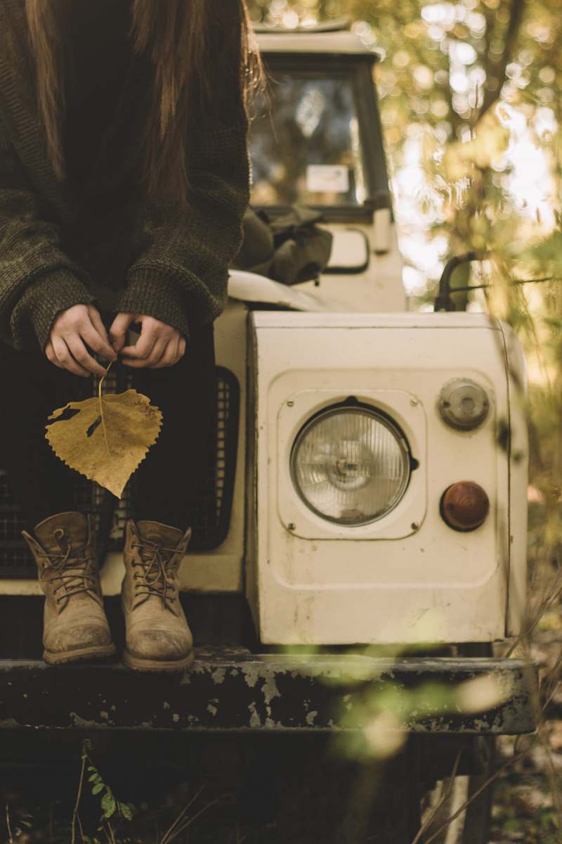 plant woman in gray sweater holding withered leaf while sitting on white vehicle jar
