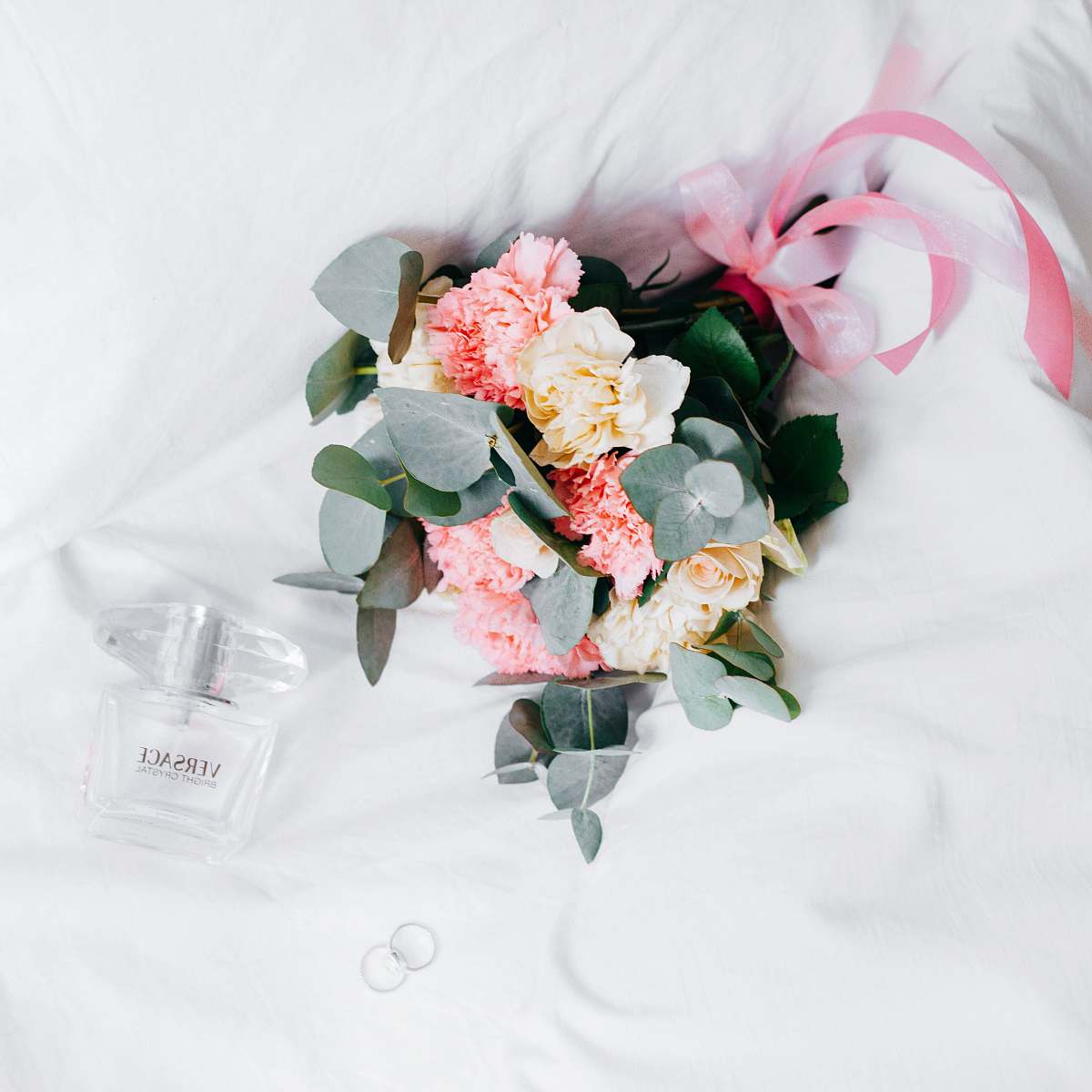 wedding bouquet of yellow-and-pink roses and chrysanthemums placed next to Versace spray bottleon white textile blossom