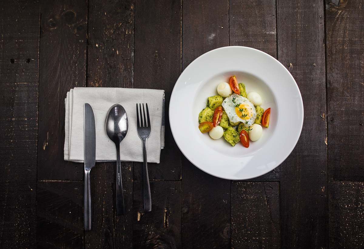 plate sunny side up egg, boiled quail eggs, sliced red tomatoes, and sliced green bell pepper inside round white ceramic plate in a fine dining set cutlery