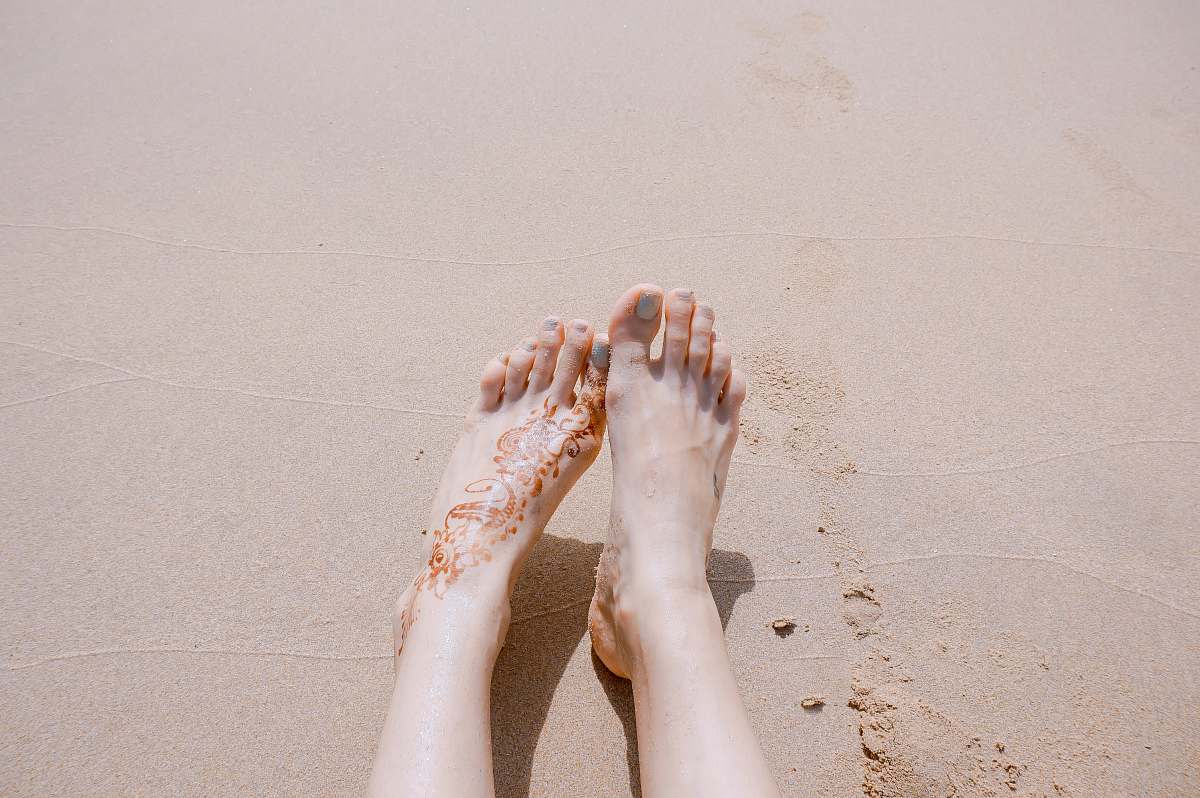 feet selective focus photography of feet with tattoo on sea sand sand