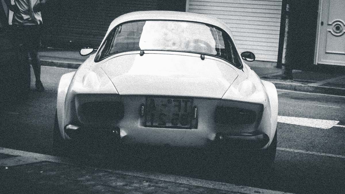 people grayscale photo of classic vehicle on road person