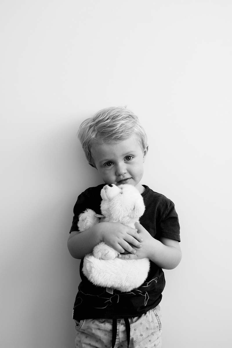 person grayscale photography of boy holding bear plush toy black-and-white