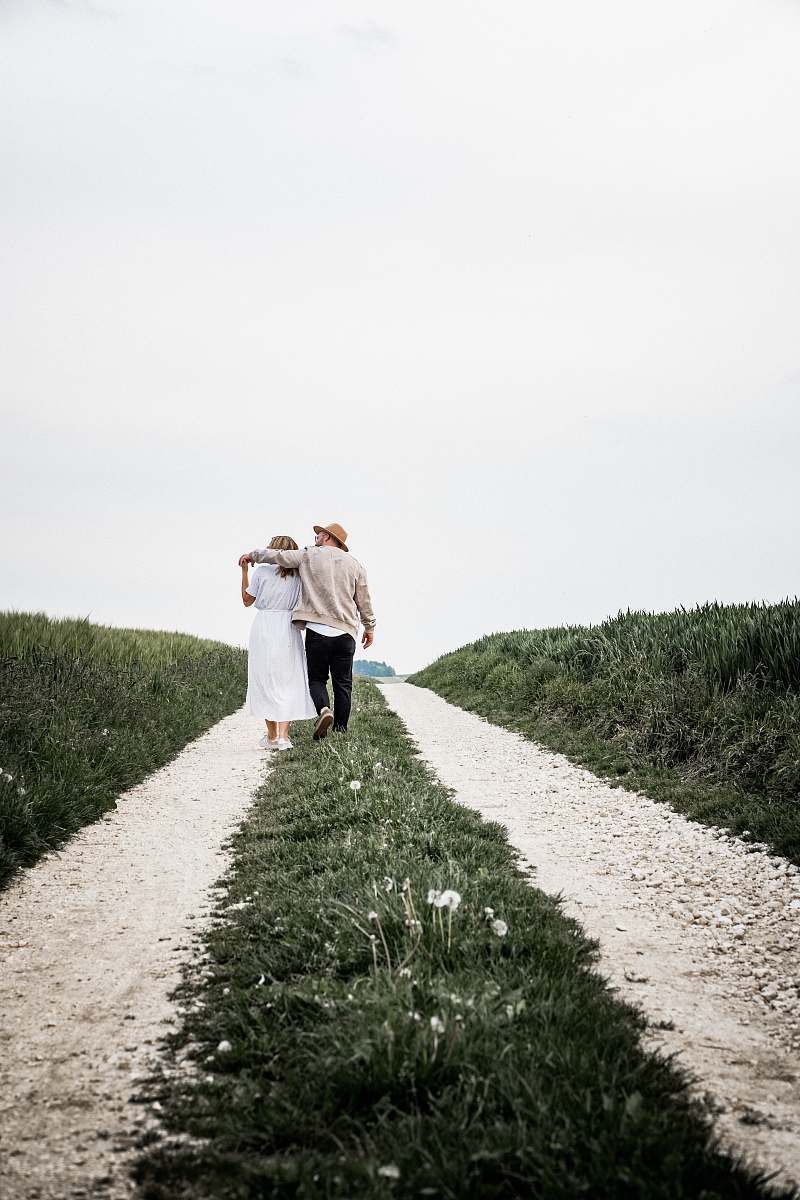 apparel man and woman walking on pathway beside green bush clothing