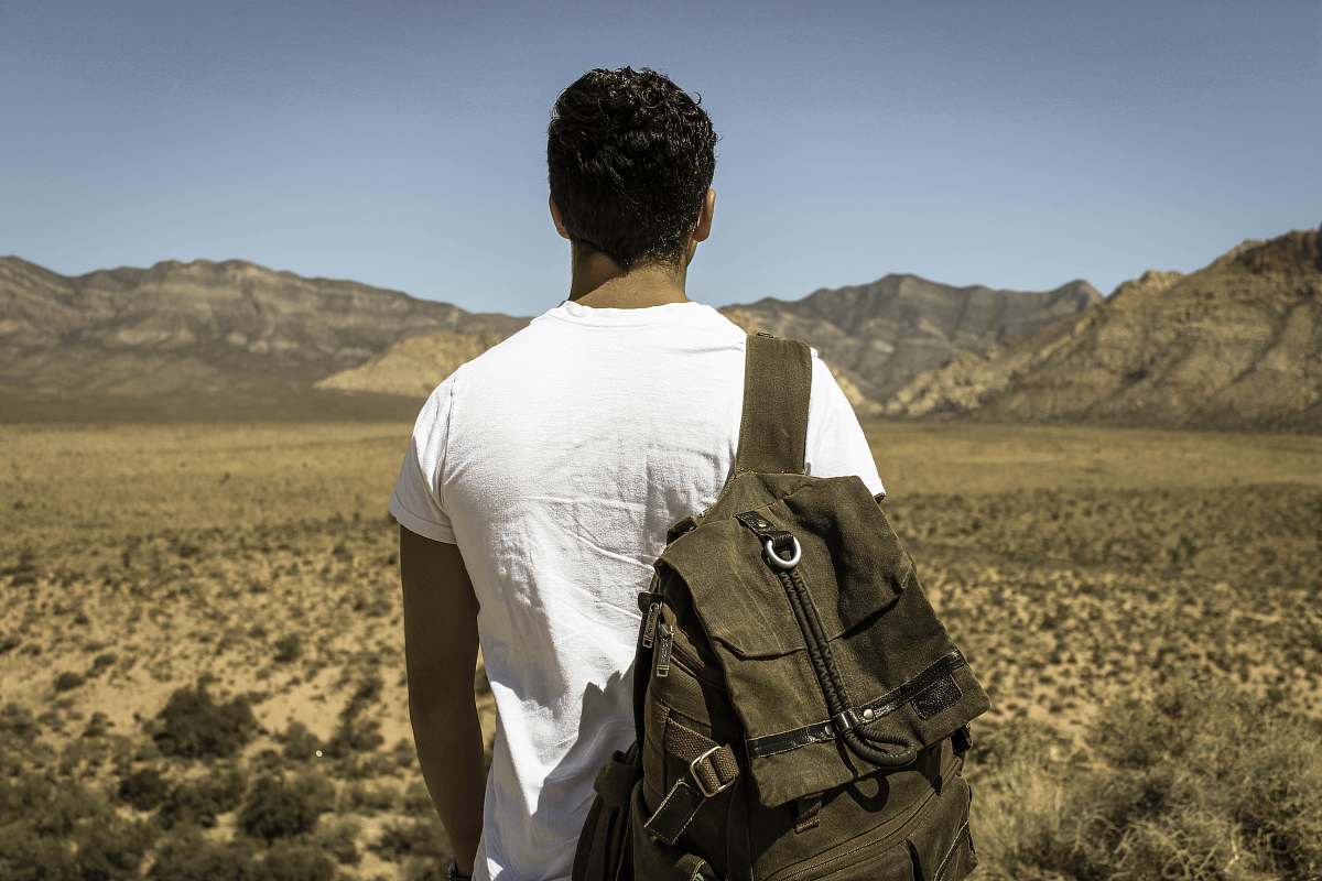 person man standing in front dried grass field near gray mountains under gray sky people