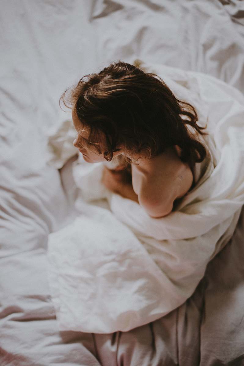 person woman sitting on bed covered with white blanket people