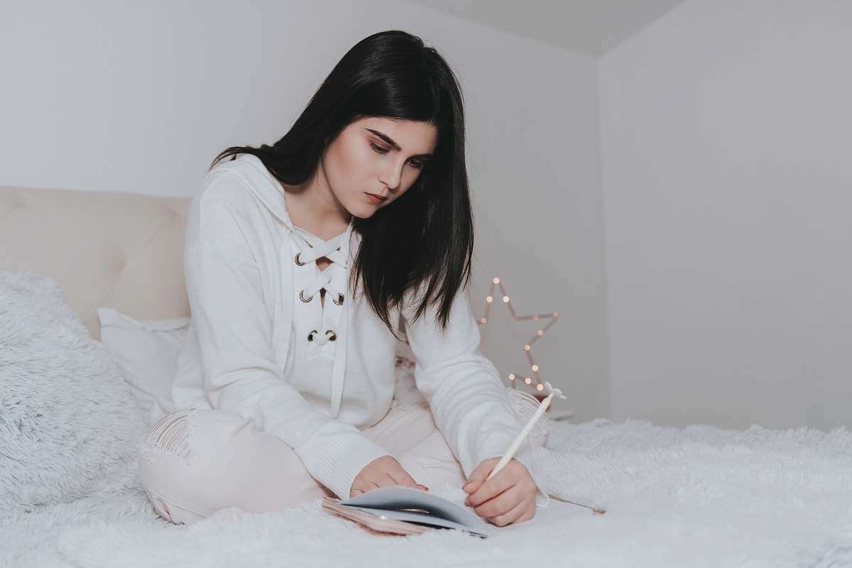 person woman sitting on bed while writing on notebook people