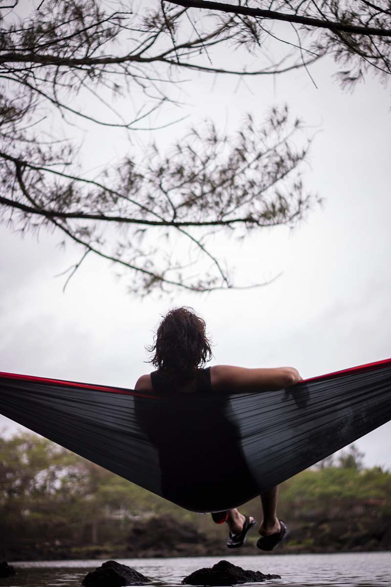 people woman sitting on hammock facing body of water person