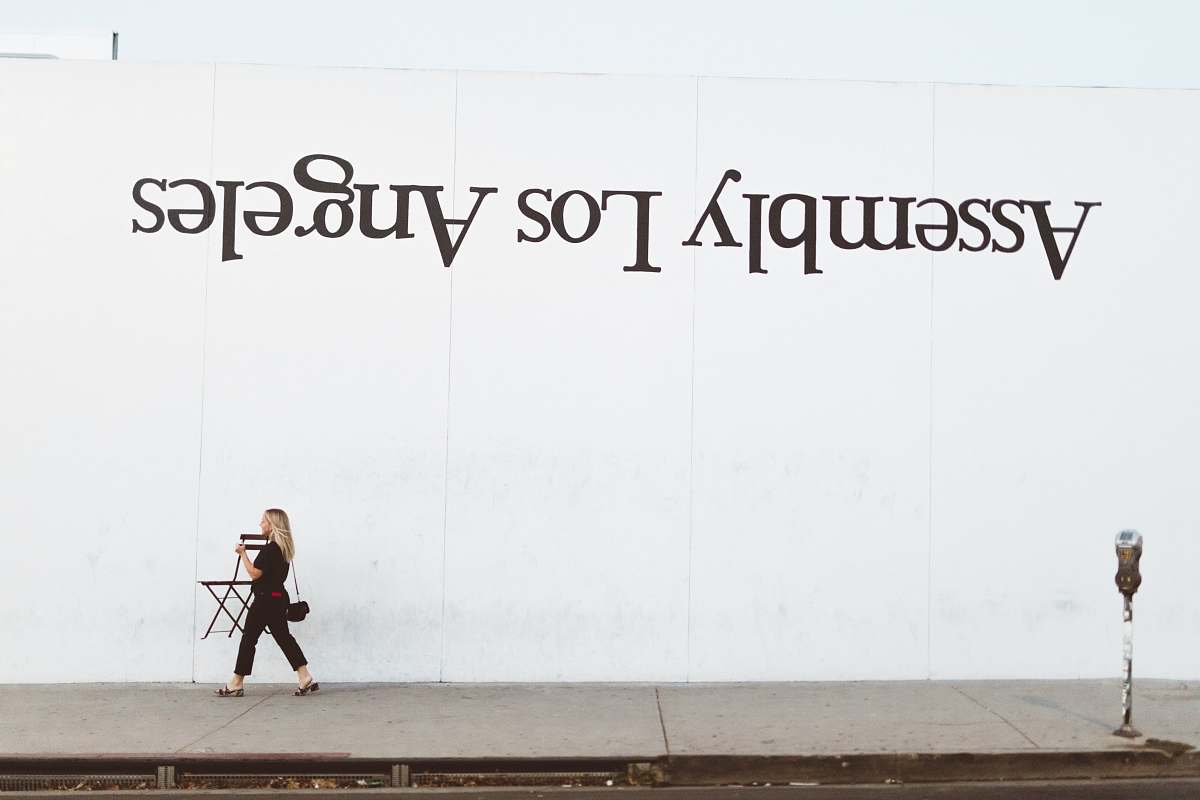 person woman walking beside white painted wall pedestrian