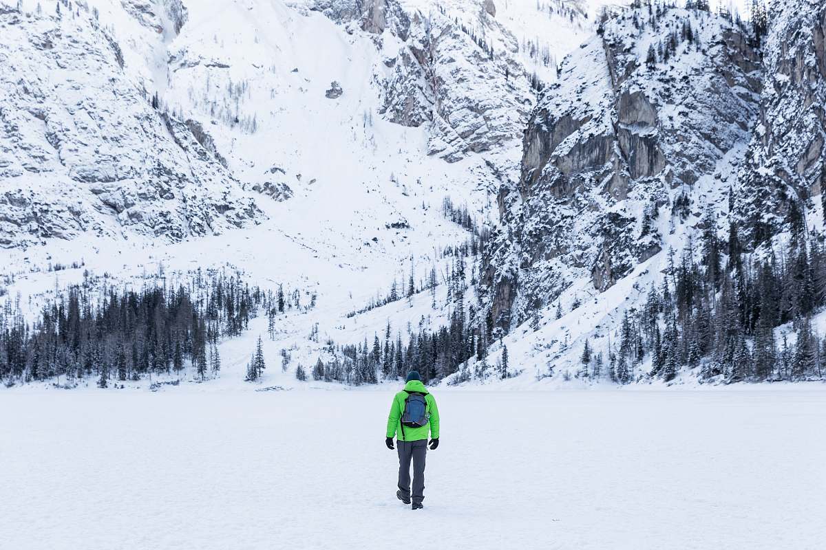 tree person in green jacket walking toward snow covered mountain braies lake