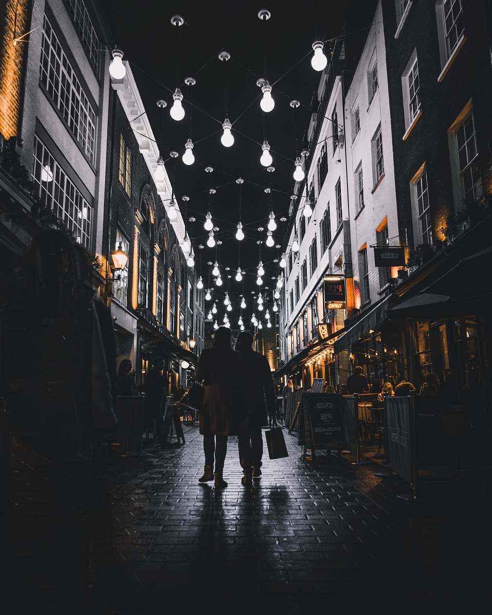 urban silhouette of couple walking under light bulbs between buildings city