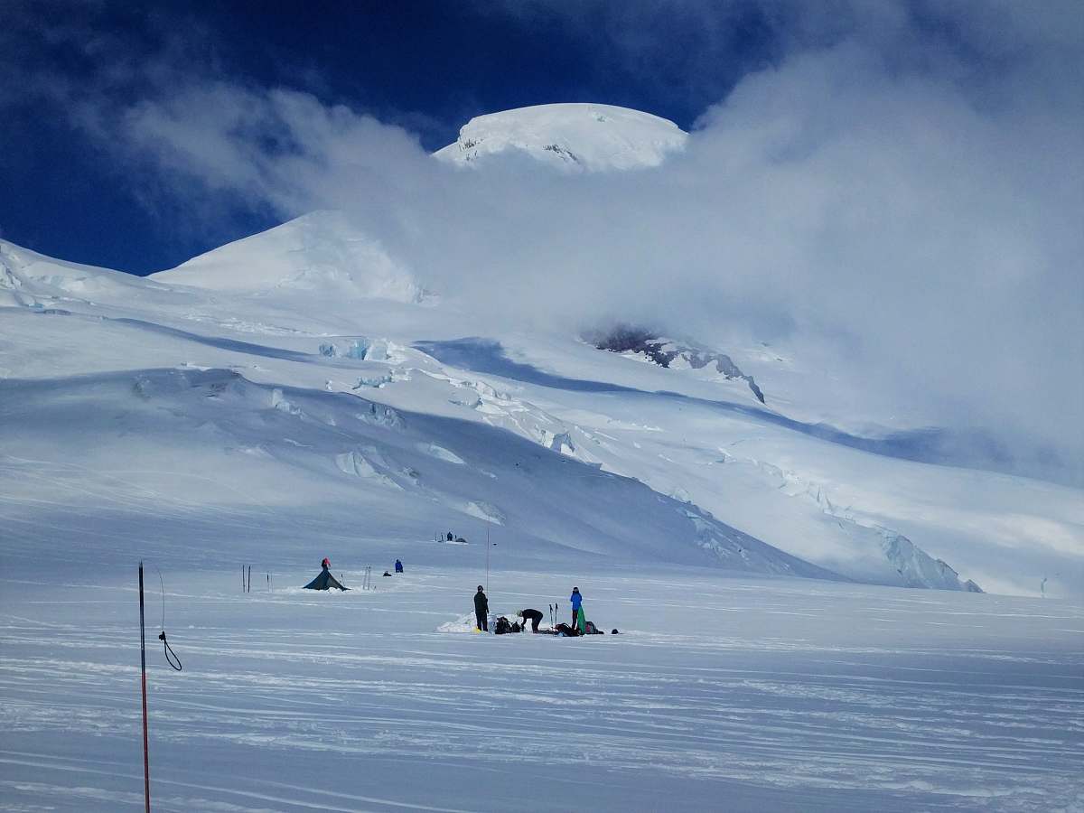 snow group of people standing on snow near tipi tent and snow covered mountain under white clouds during daytime glacier