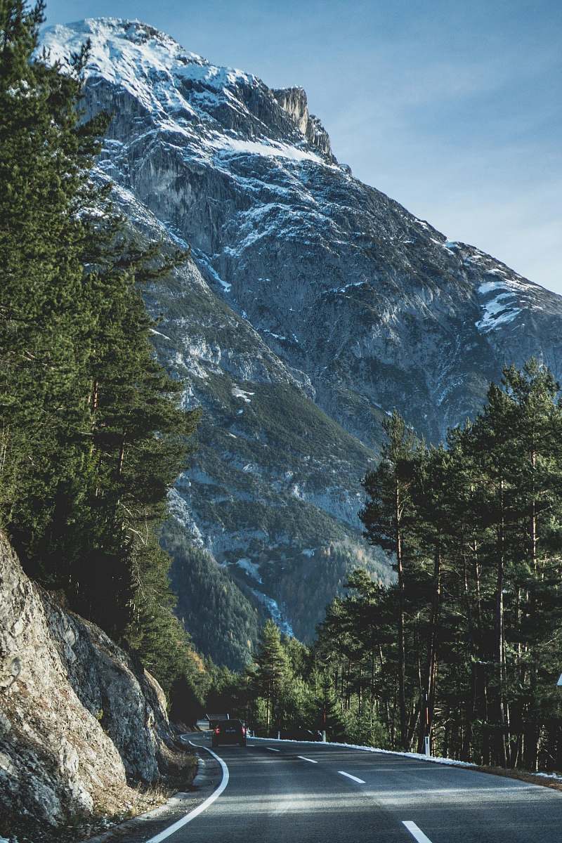 snow photograph of concrete road between trees and cliff with mountain background glacier