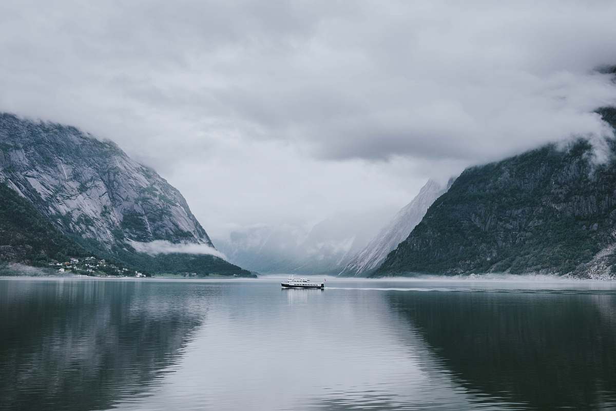 snow white and gray boat in the middle of calm body of water near mountain under white sky nature