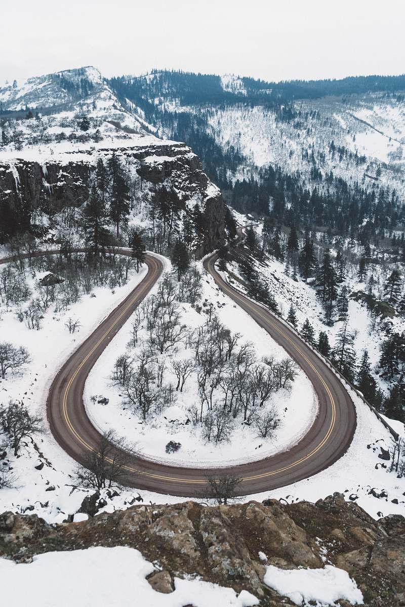 mountain aerial photography of curved road in between snow covered ground overlooking mountain and trees under white sky at daytime trees