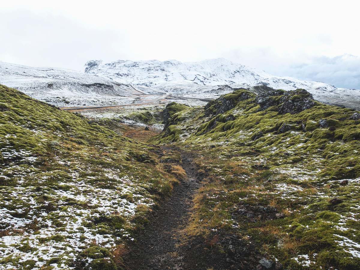 mountain pathway between green grass hill towards snow capped mountain outdoors