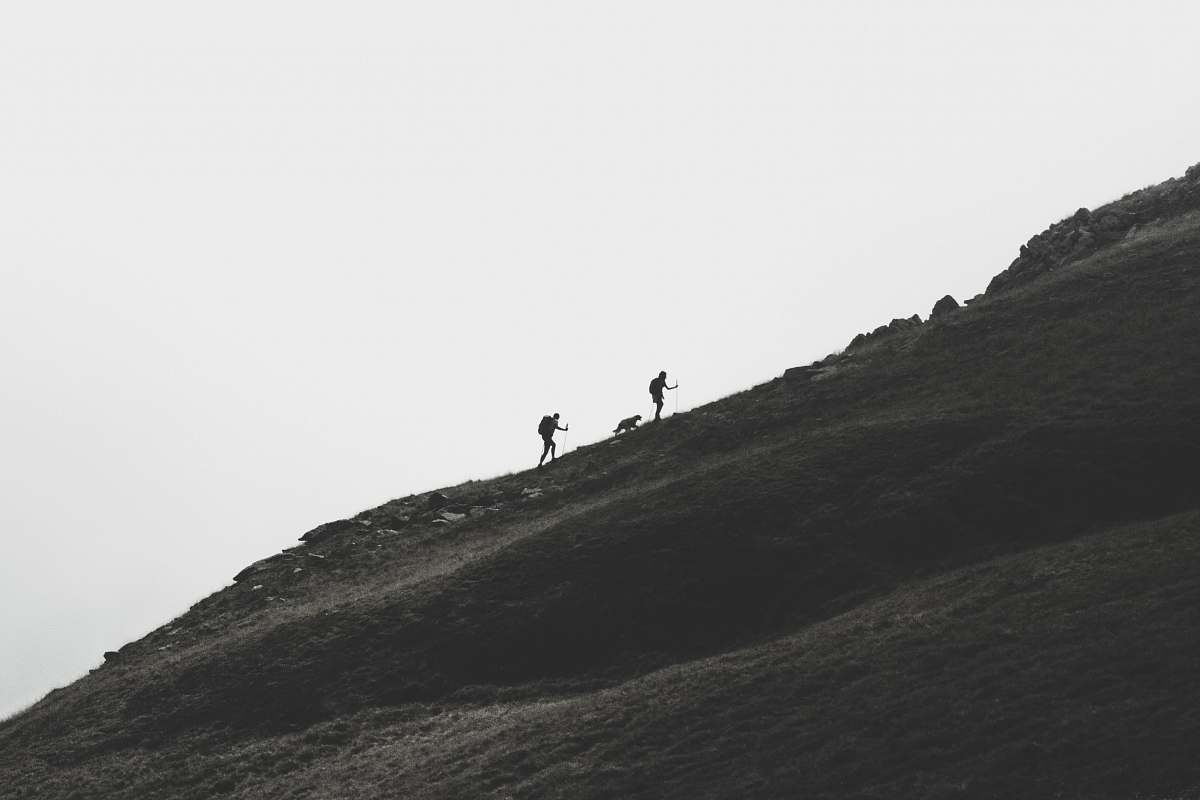 black-and-white silhouette of person walking on mountain slope