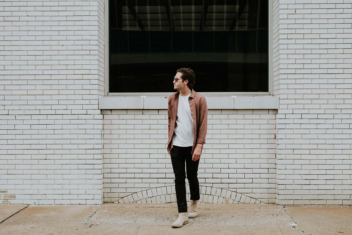 human man standing beside beige brick wall person