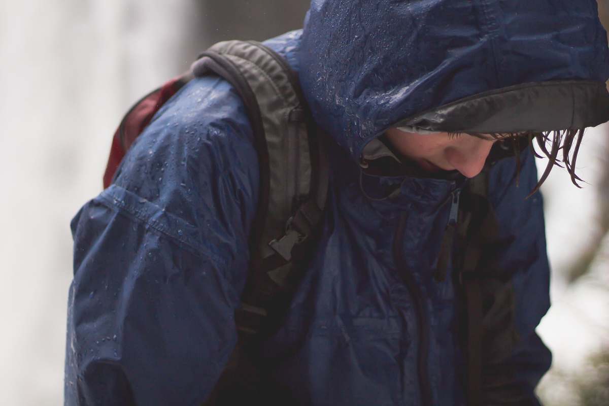 human person in blue raincoat and black backpack walking with head low person