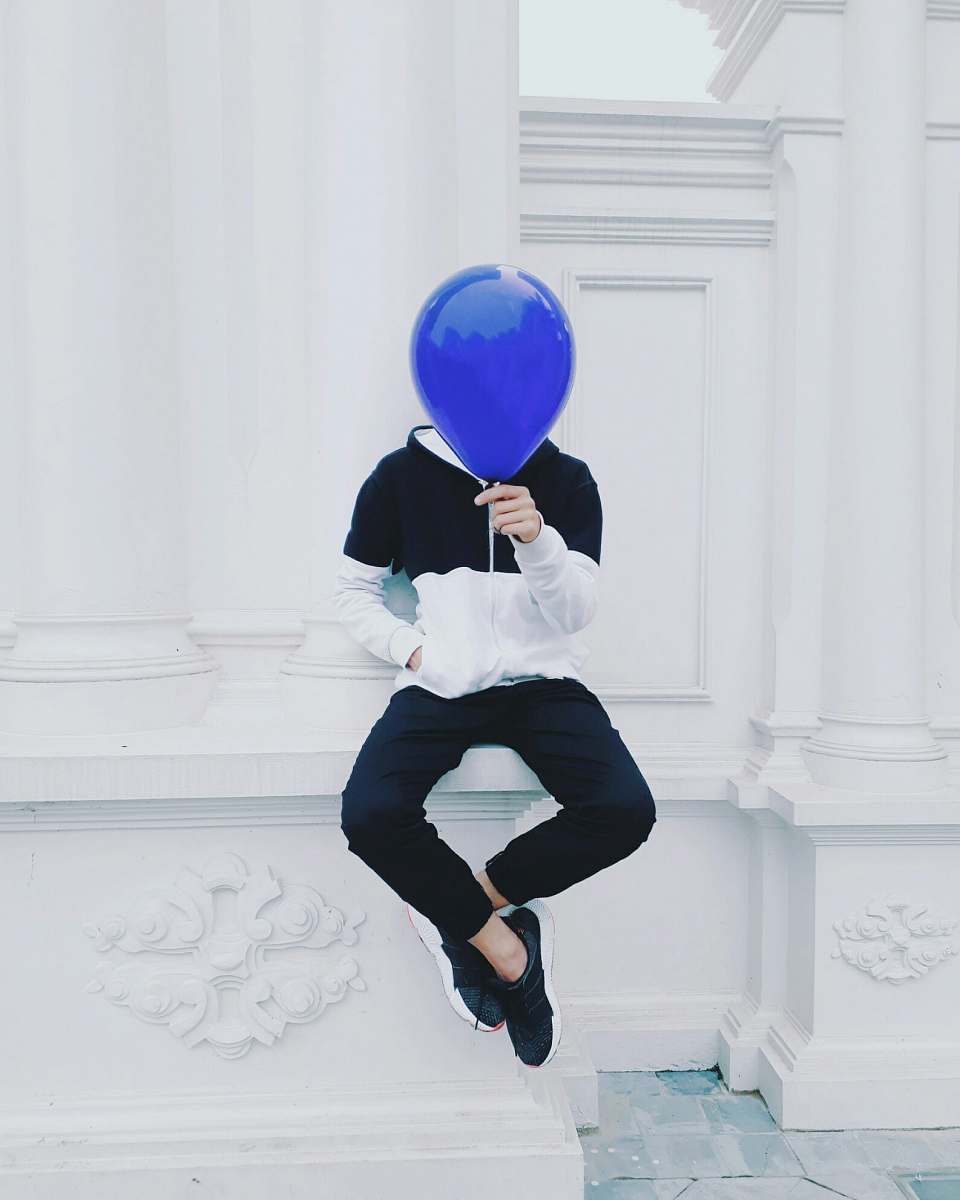 person person sitting on white concrete pavement holding blue balloon at daytime human