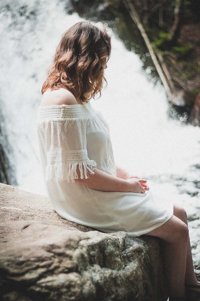 person woman sitting on rock beside waterfall at daytime human