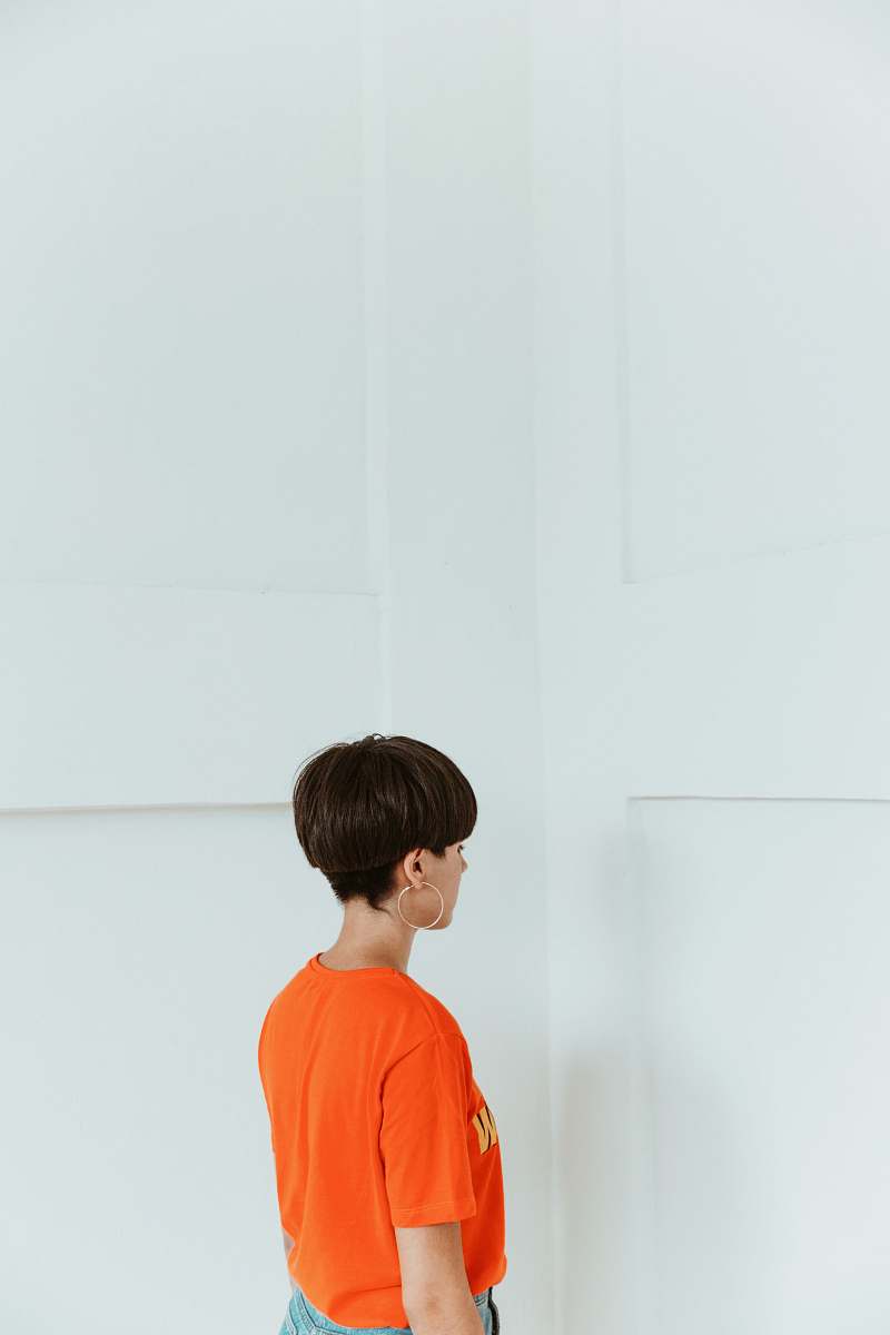 human woman wearing orange shirt facing white wall person