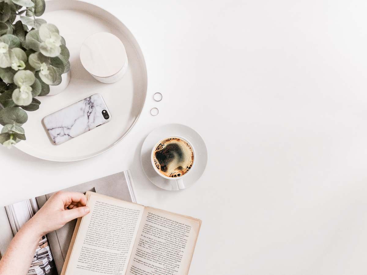 page flat-lay photography of person holding opened book on tabletop beside cup of black coffee text