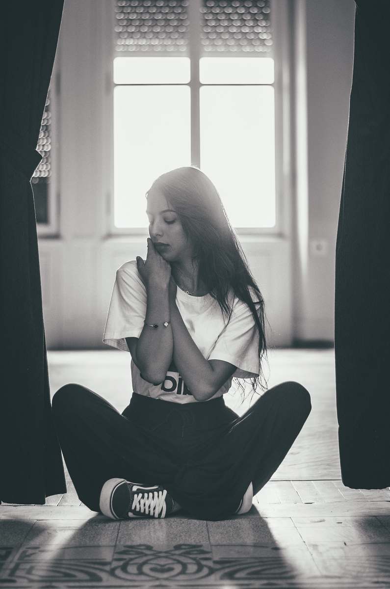human gray scale photography of woman sitting near between curtain people