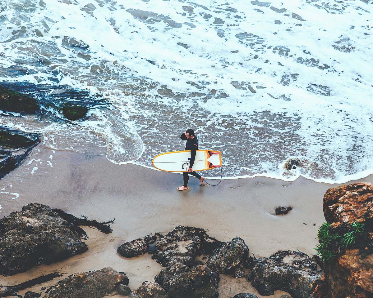 surfboard man holding surfboard walking on seashore during daytime people
