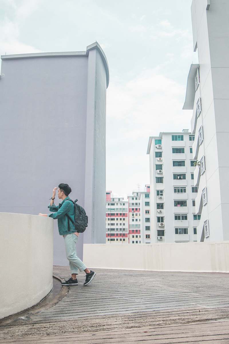 human man in teal jacket standing beside white concrete fence people