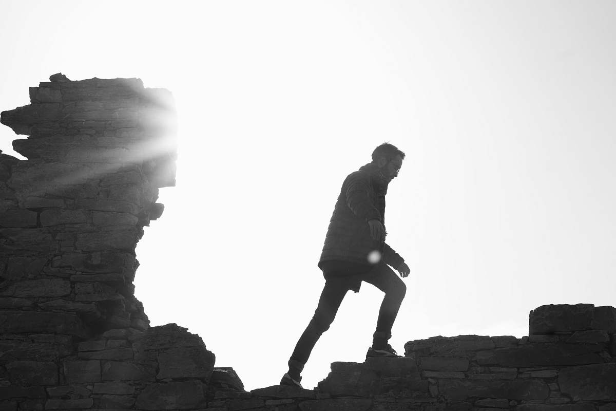 black-and-white man wearing jacket walking on brick wall human