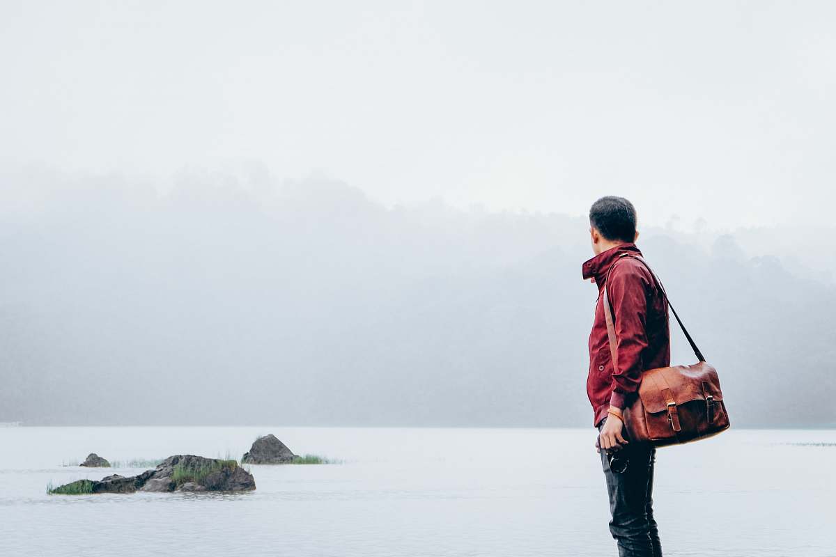 human man with messenger bag looking towards the sea people