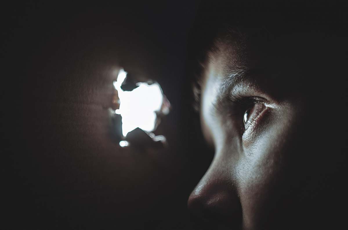 dark person watching through hole light