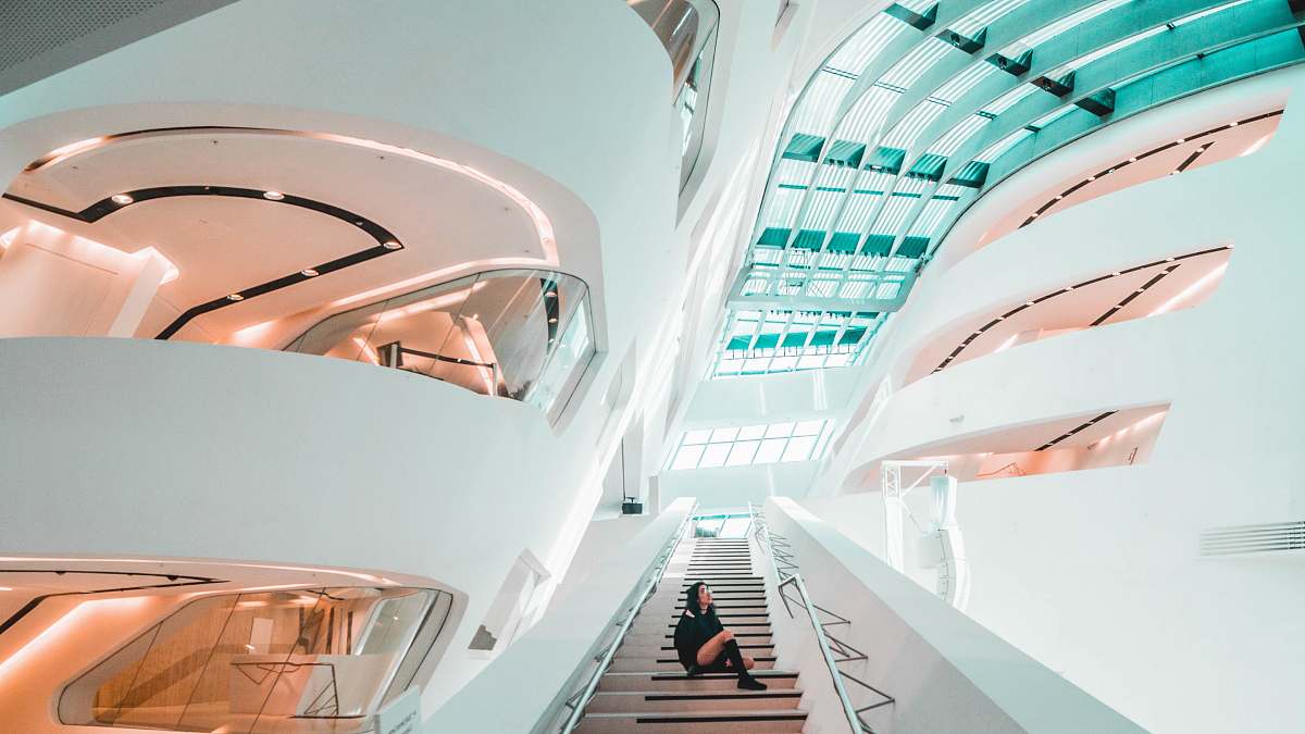 modern sitting woman on stairs inside white concrete building handrail