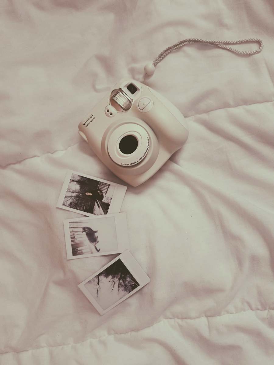 human white Fujifilm instant camera on white comforter people