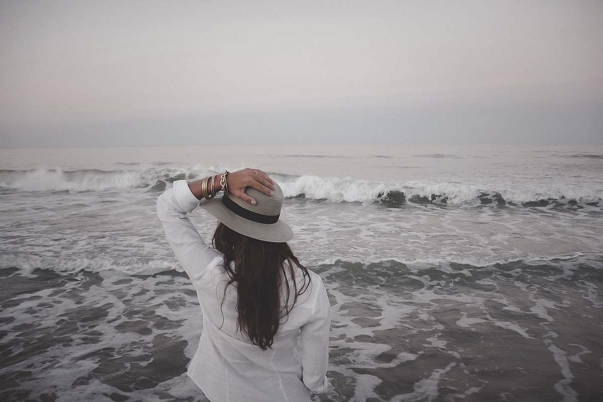 people woman holding hat beside body of water beach