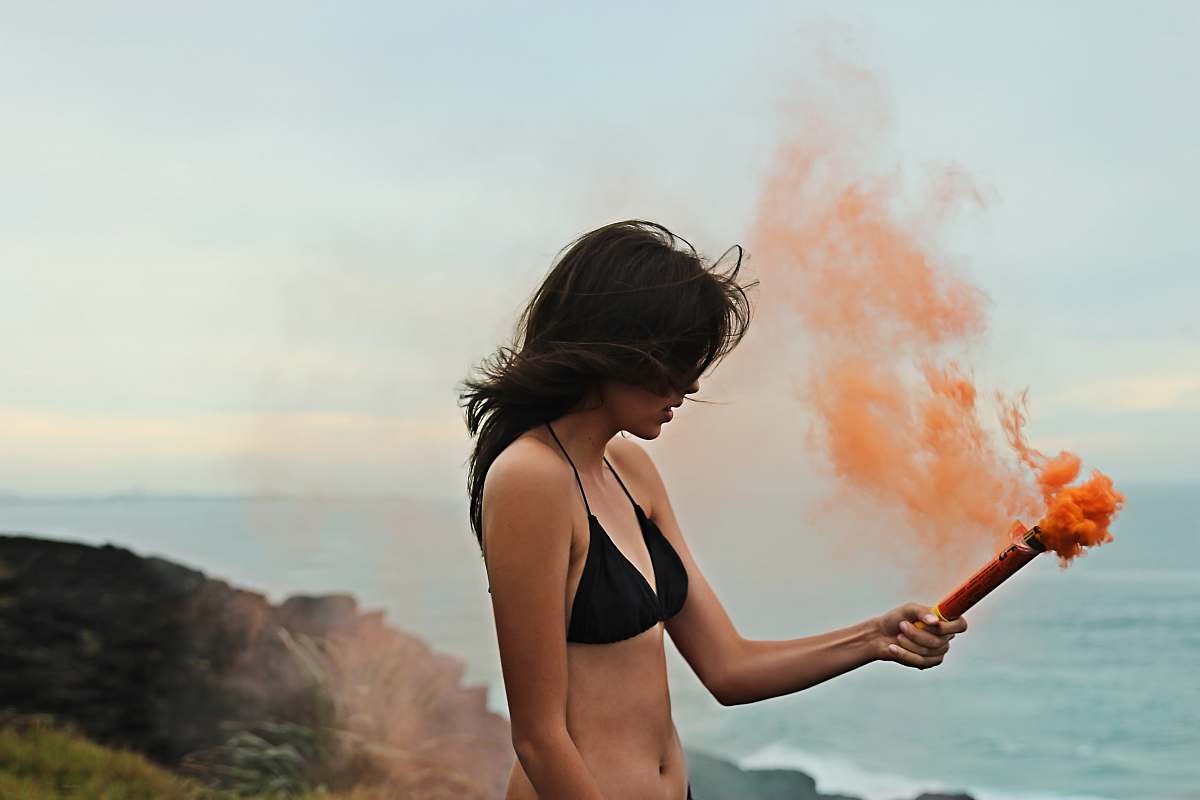 human woman in black bikini holding orange smoke apparel