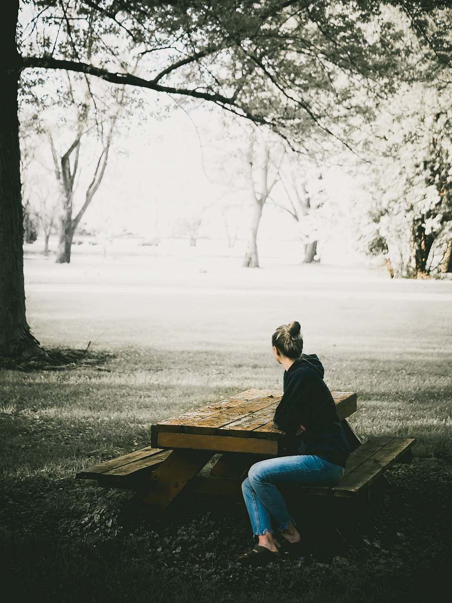 human woman in black hoodie and blue denim jeans sitting on picnic bench sitting