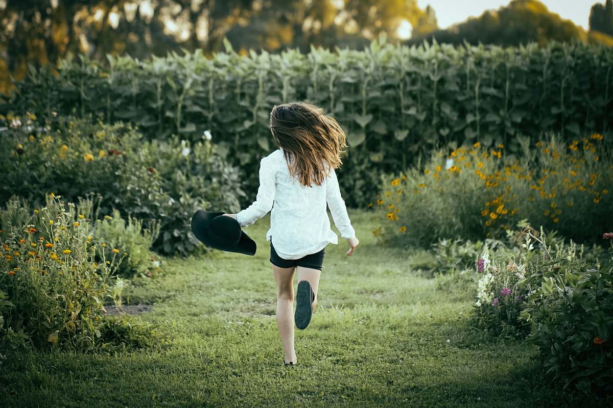 human woman running on grass surrounded with flowers during daytime people