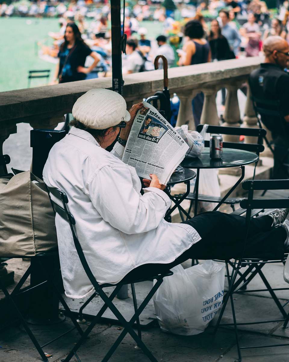 human woman sitting on chair while reading a newspaper near body of water people