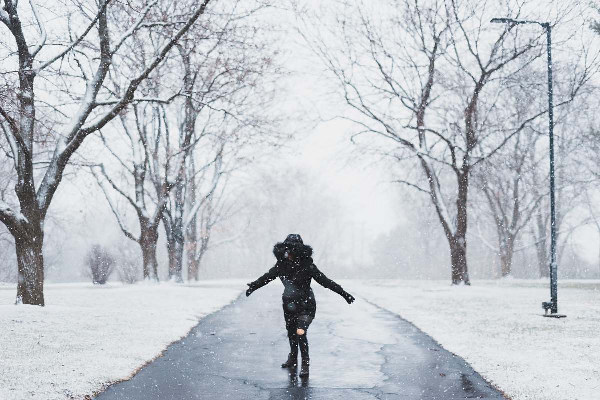 people woman wearing black parka jacket standing on road near tall trees and light post during daytime human