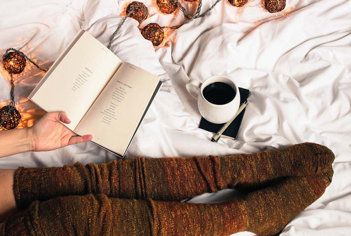 book mug of black coffee beside person's feet wearing brown stockigns coffee