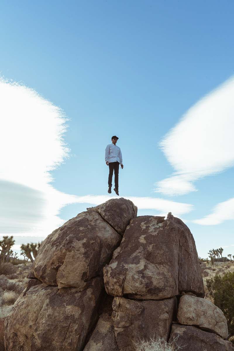 blue man jump on brown boulder joshua tree