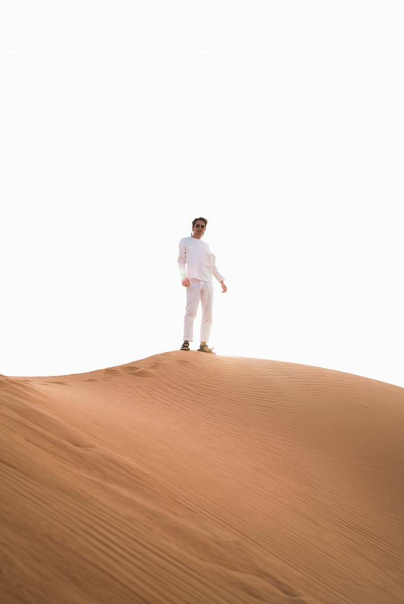 white man standing atop desert sand dune desert
