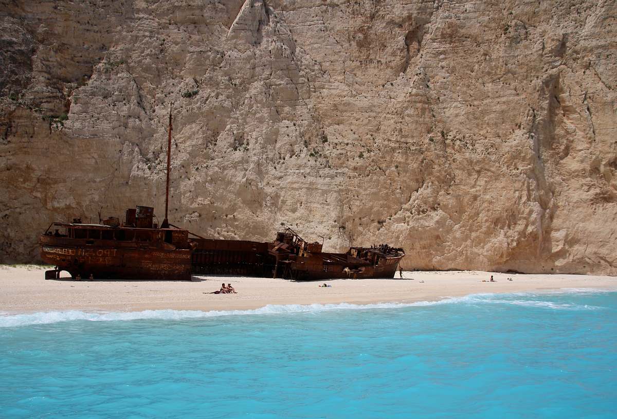 shipwreck group of people on seashore near ship near mountain at daytime greece