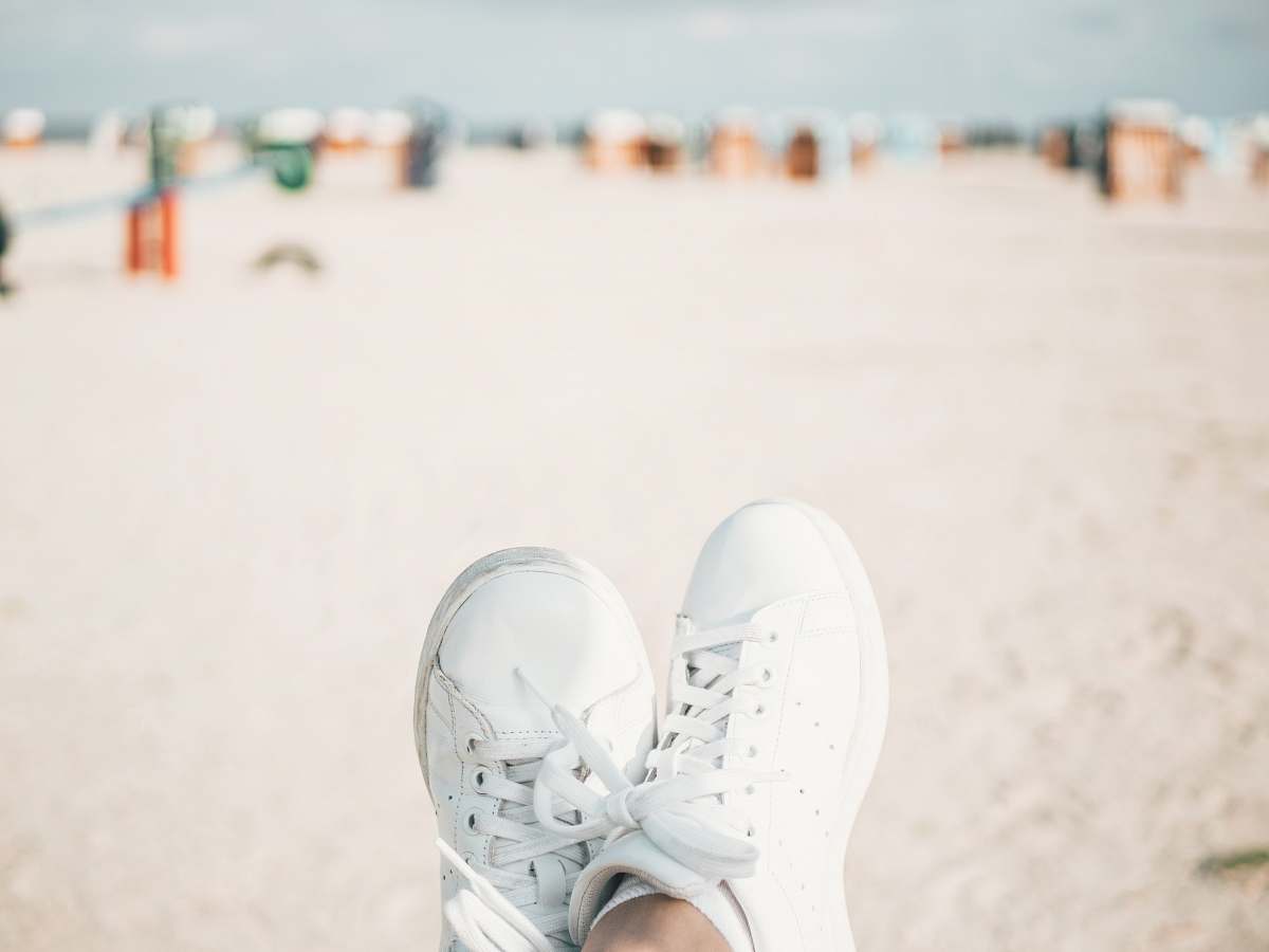 brown person wearing pair of white adidas low-top lace-up shoes sneaker
