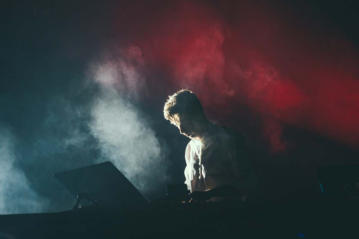 music A musician in a white shirt on stage with white and red lights breaking through the smoke behind his back man
