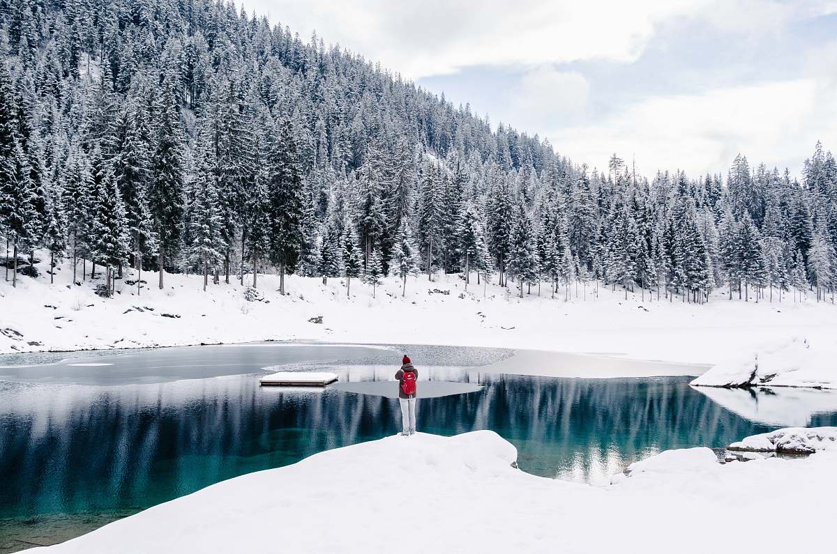 winter person standing beside body of water surrounded by snow field near trees outdoors
